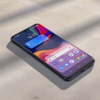 Google Pixel 10 Pro lying flat on a warm grey concrete surface, screen showing Android 17 home screen with a floating app bubble overlay visible, cinematic side lighting from the left with soft long directional shadows, no hands, no people, no text, sharp focus, photorealistic, 16:9