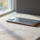 Samsung Galaxy S26 Ultra resting flat on a warm grey concrete surface, rear panel visible showing camera system and titanium frame, shot at 45-degree angle, 50mm lens, shallow depth of field, soft natural window light from the left, long diffused shadows, no hands, no people, no text, no watermark, sharp focus, photorealistic, 16:9